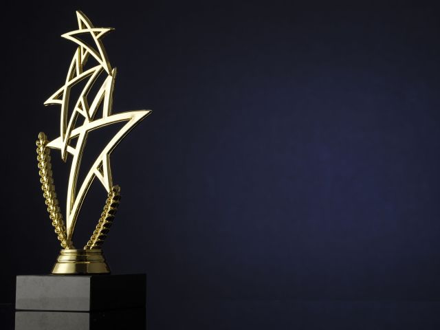 Stylish trophy with three gold stars and laurel wreath for the winner of a championship or competition over a dark background and copyspace