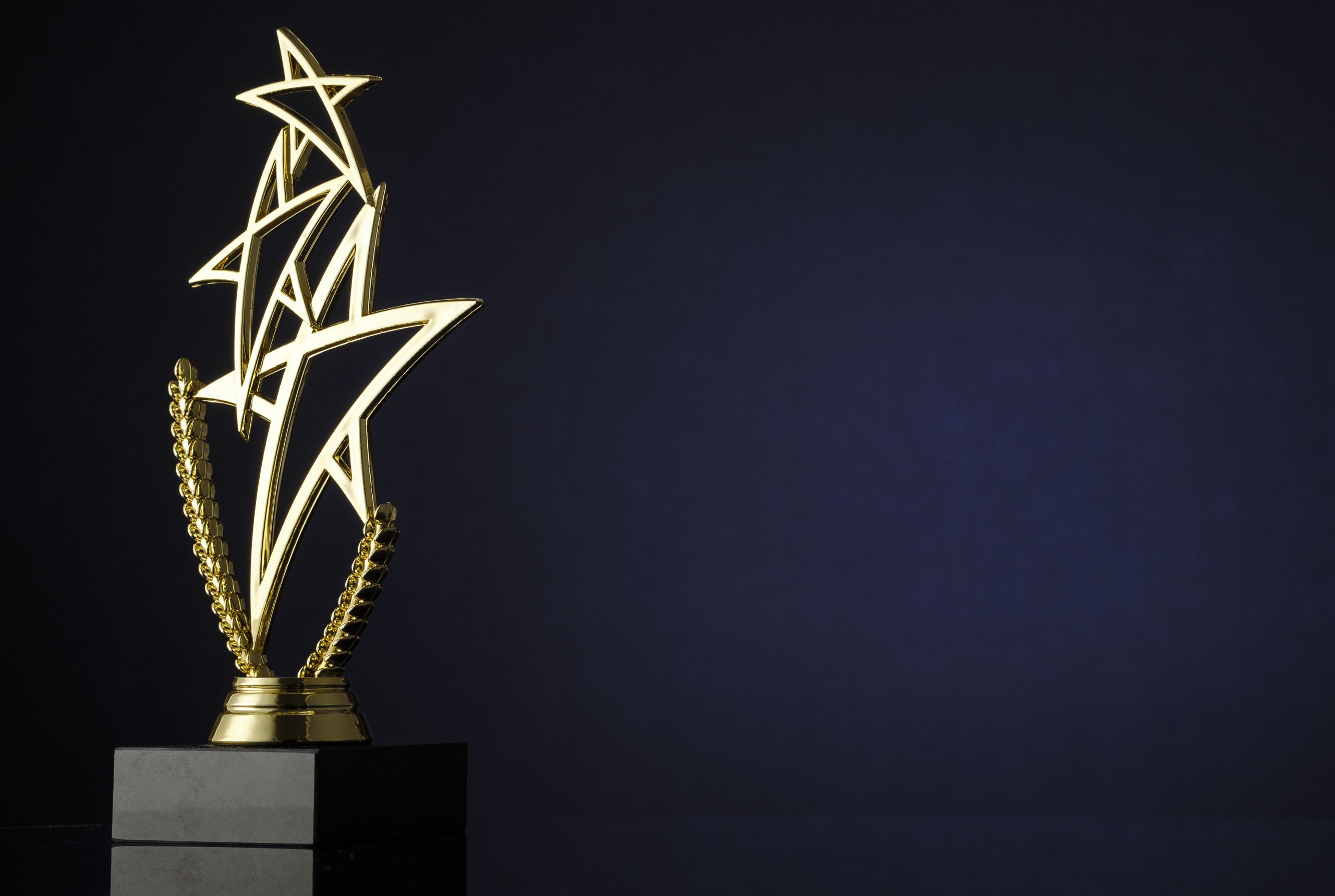 Stylish trophy with three gold stars and laurel wreath for the winner of a championship or competition over a dark background and copyspace